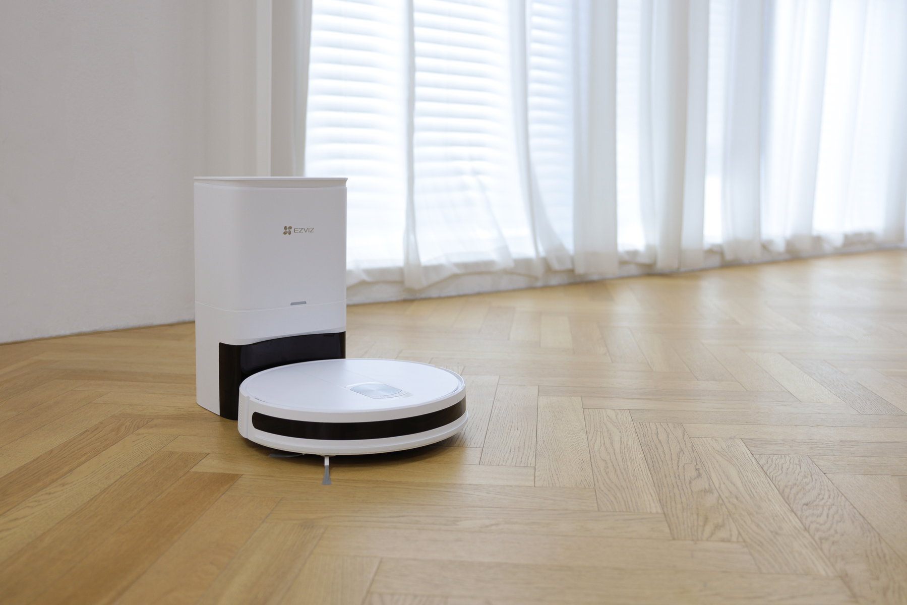 Ein weißer Roboter-Staubsauger und seine Ladestation auf einem Holzboden.