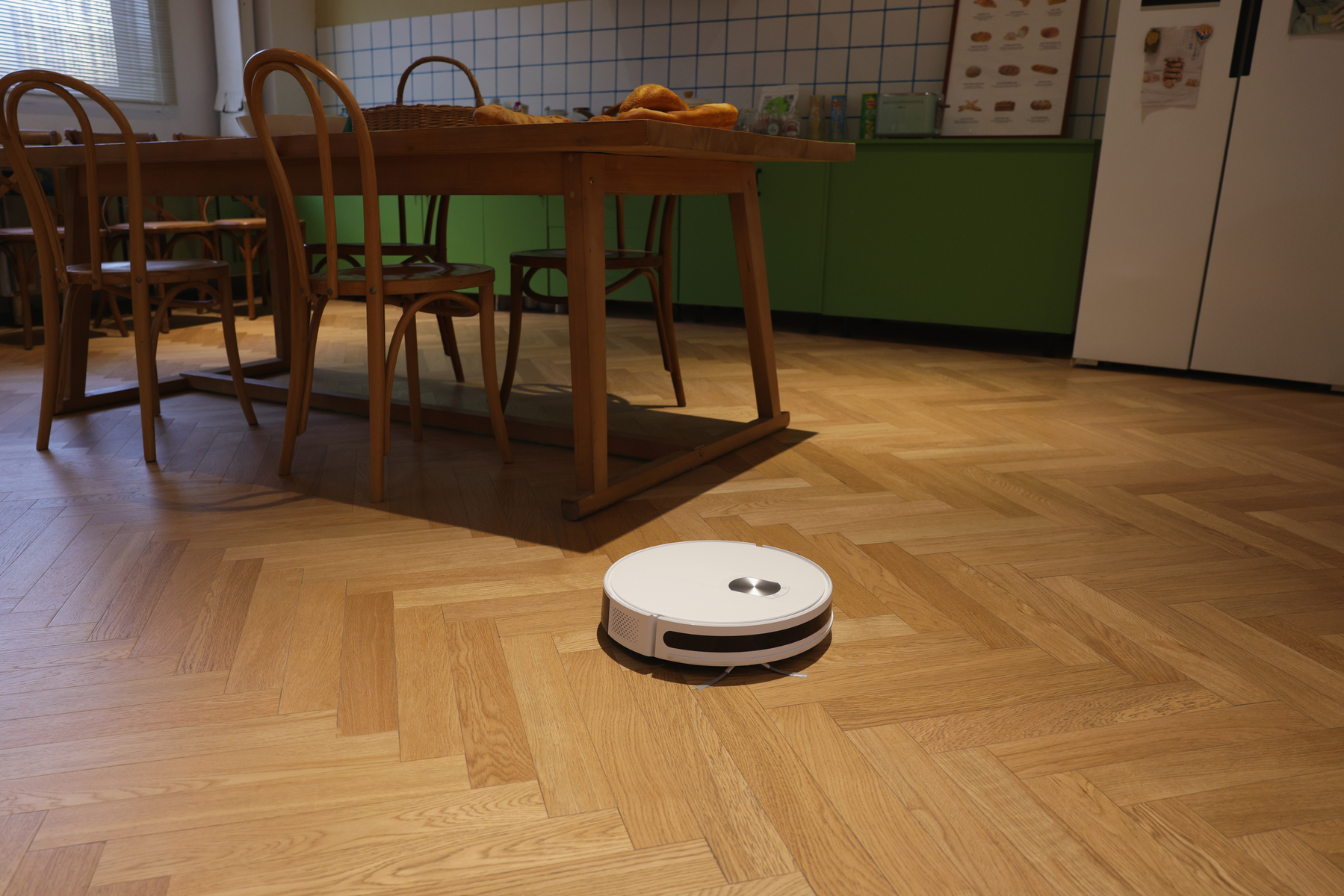 Ein Roboter-Staubsauger auf einem hellen Holzboden in einer Küche.