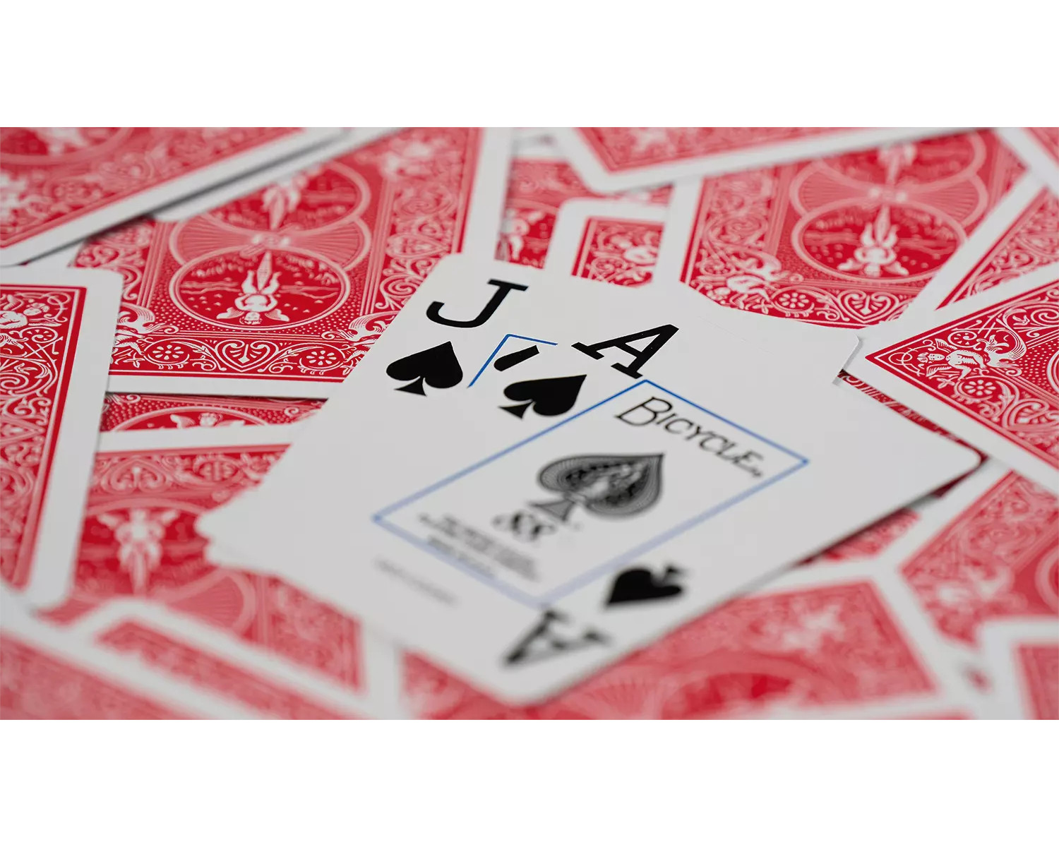 Spielkarten mit Pik-Bube und Pik-Ass offen. Rote Kartenrücken sind sichtbar.