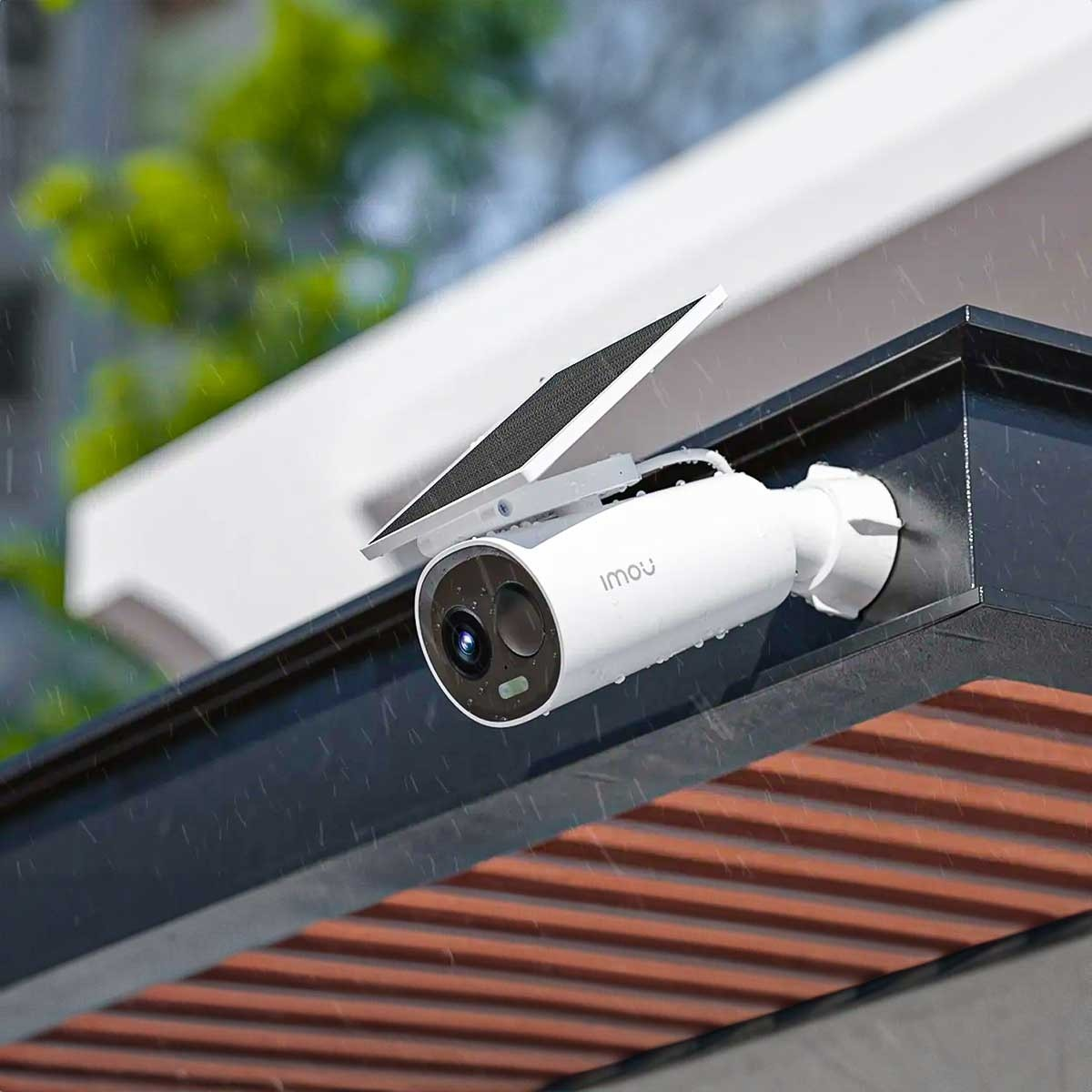 Biała kamera bezpieczeństwa z panelem słonecznym. Zamontowana na ciemnym dachu, pada deszcz.