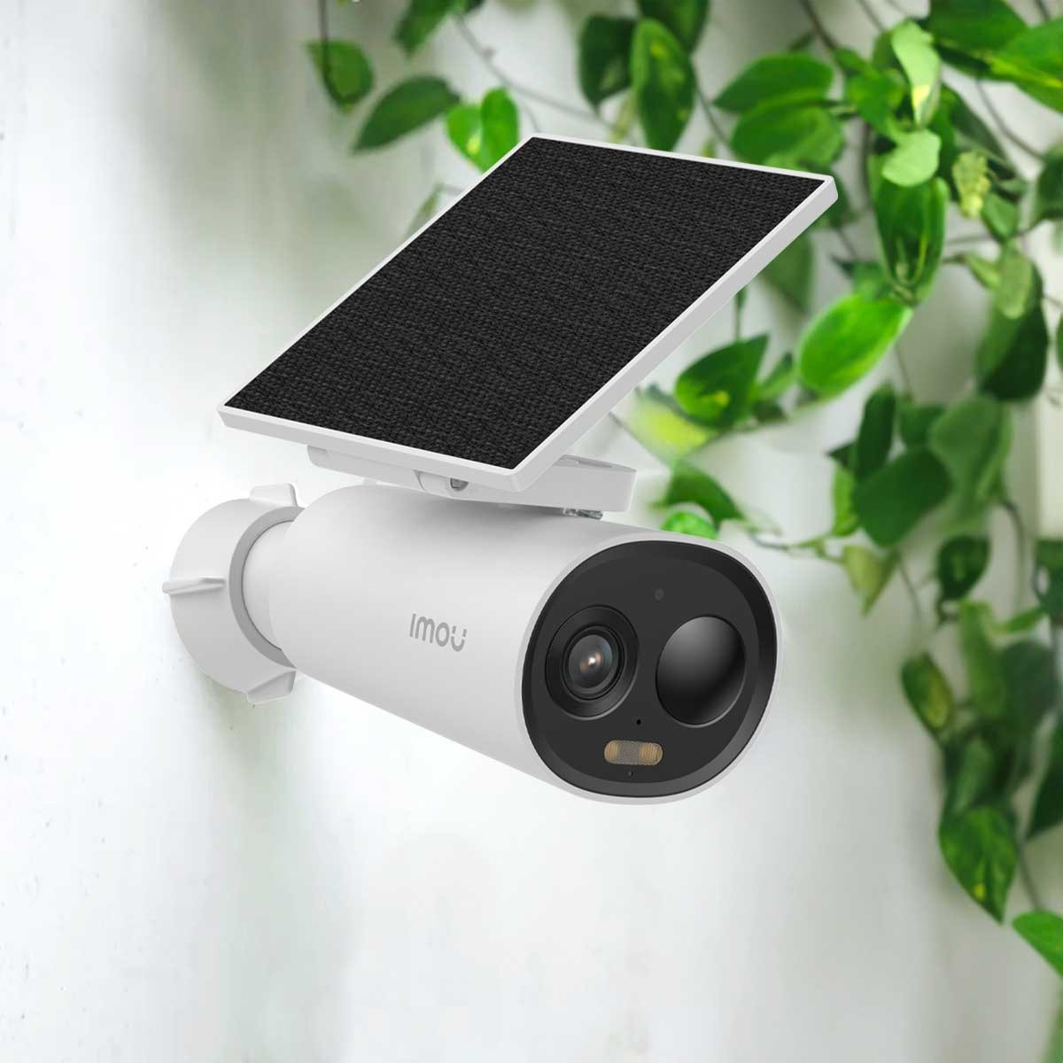 Biała kamera bezpieczeństwa z panelem słonecznym. Zamontowana na ścianie, z zielenią w tle.