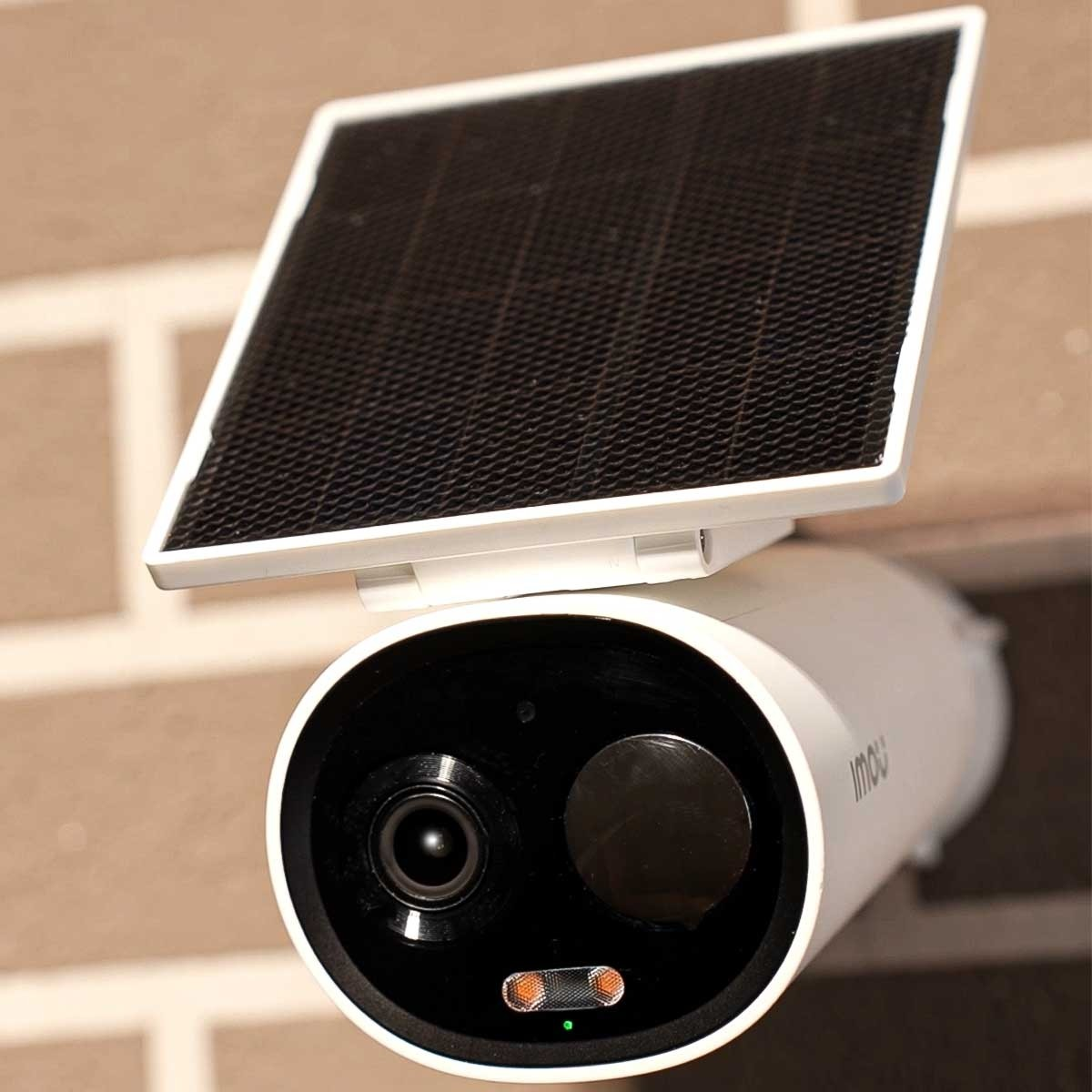 Biało-czarna kamera bezpieczeństwa z panelem słonecznym na ceglanej ścianie.