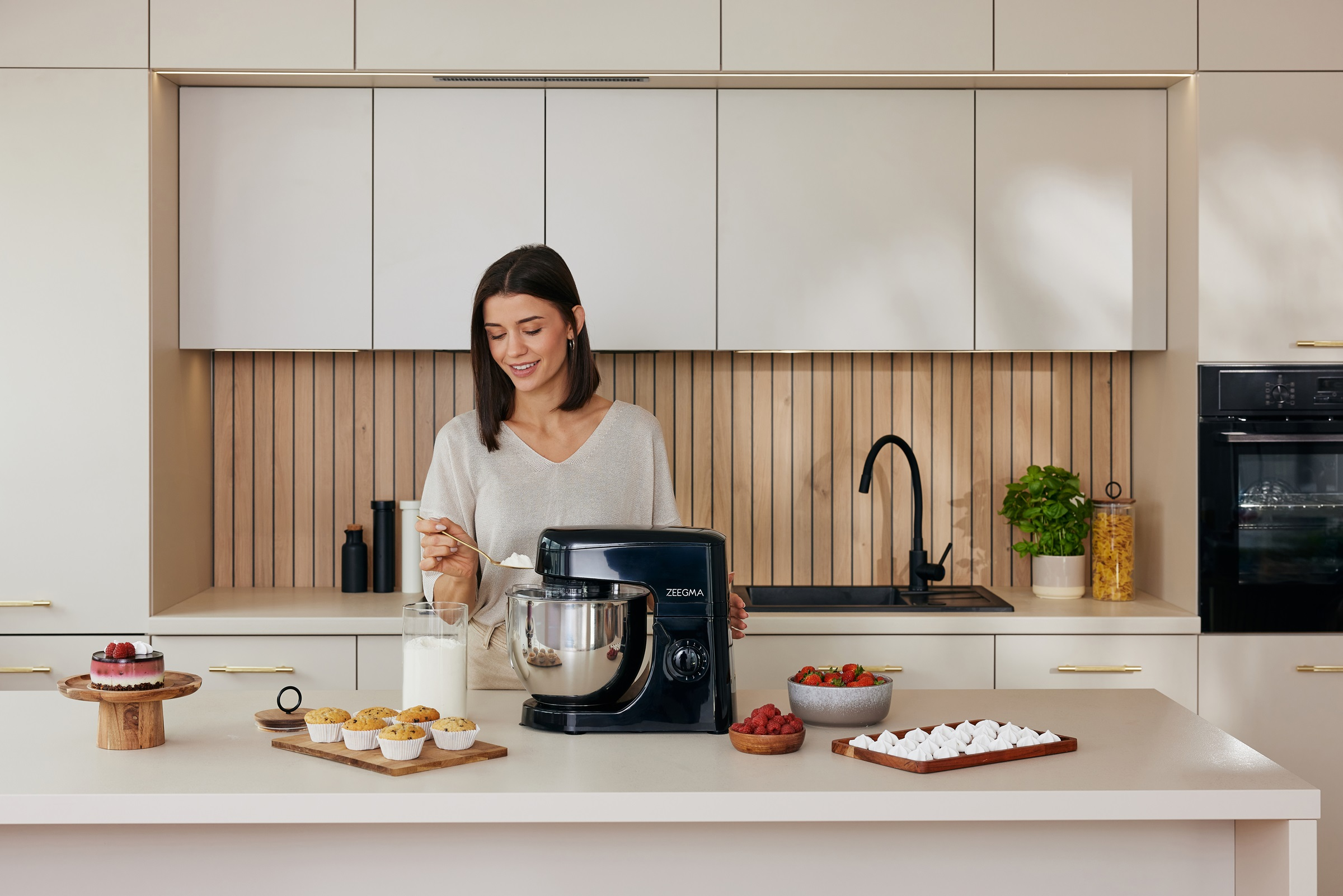 Kobieta w kuchni, piecze z mikserem. Różne wypieki i składniki na blacie.