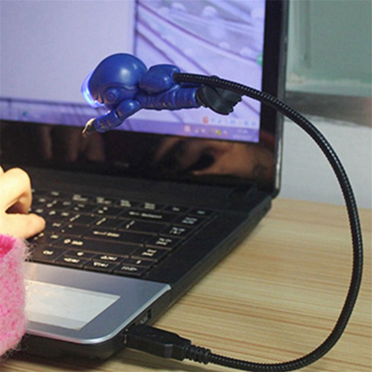 Ein blaues USB-Licht in Astronautenform ist an einen Laptop angeschlossen. Eine Hand berührt den Laptop.
