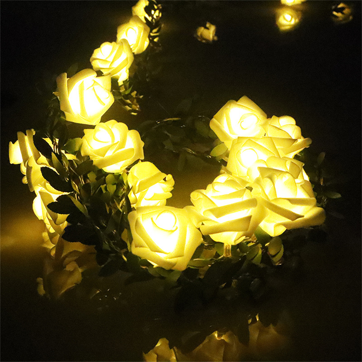 Girlande aus beleuchteten weißen rosenförmigen Lichtern mit grünen Blättern, auf dunklem Hintergrund.