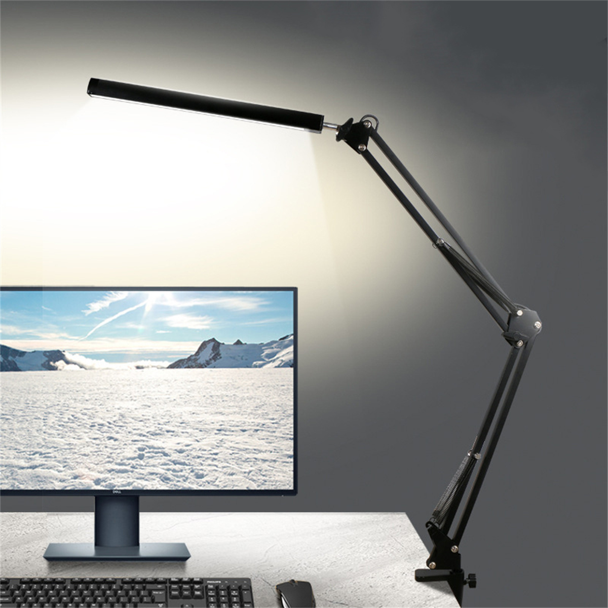 Eine schwarze Schreibtischlampe mit verstellbarem Arm steht auf einem Schreibtisch. Monitor und Tastatur sind sichtbar.