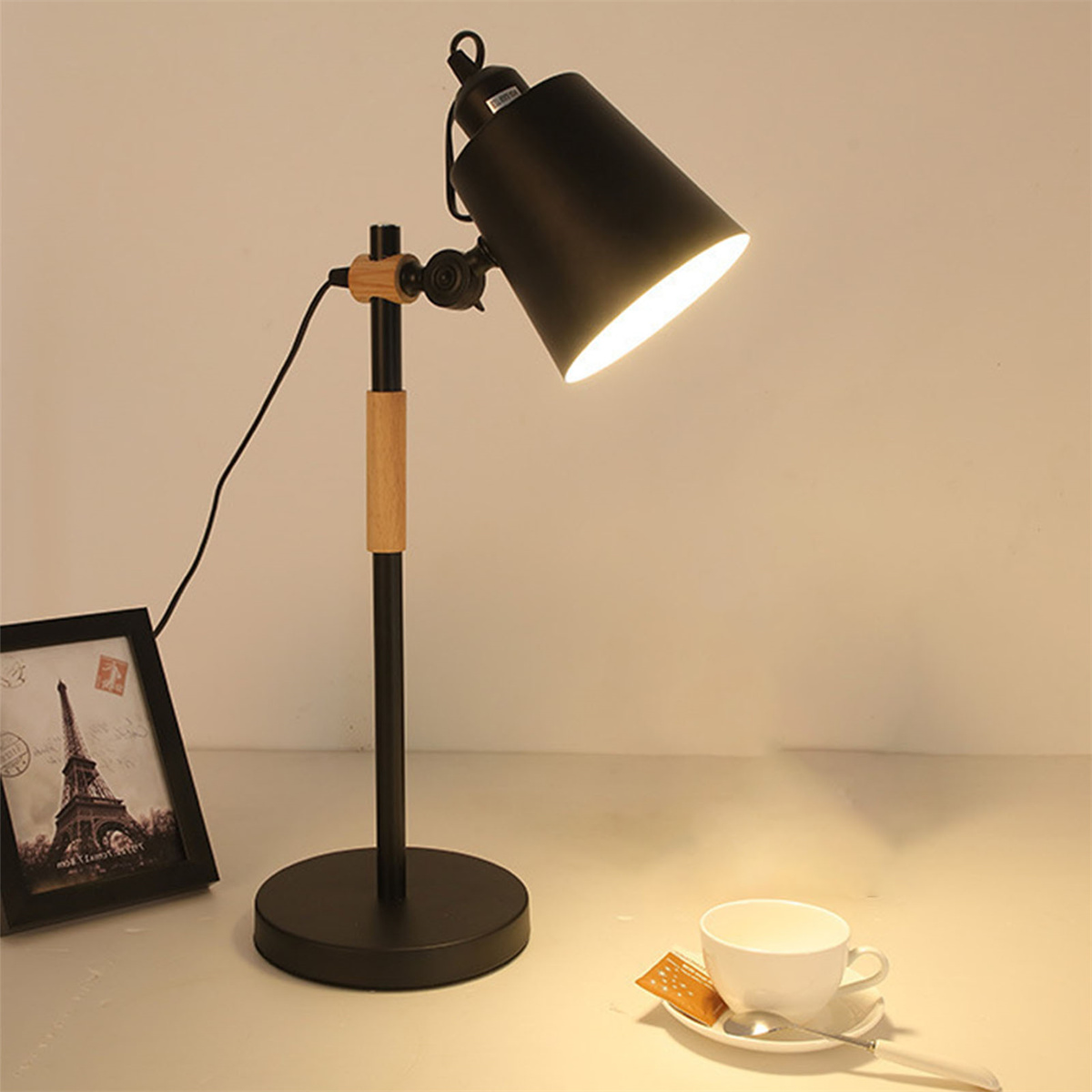 Schwarze Schreibtischlampe mit Holzakzenten auf weißer Oberfläche, neben einer Tasse.