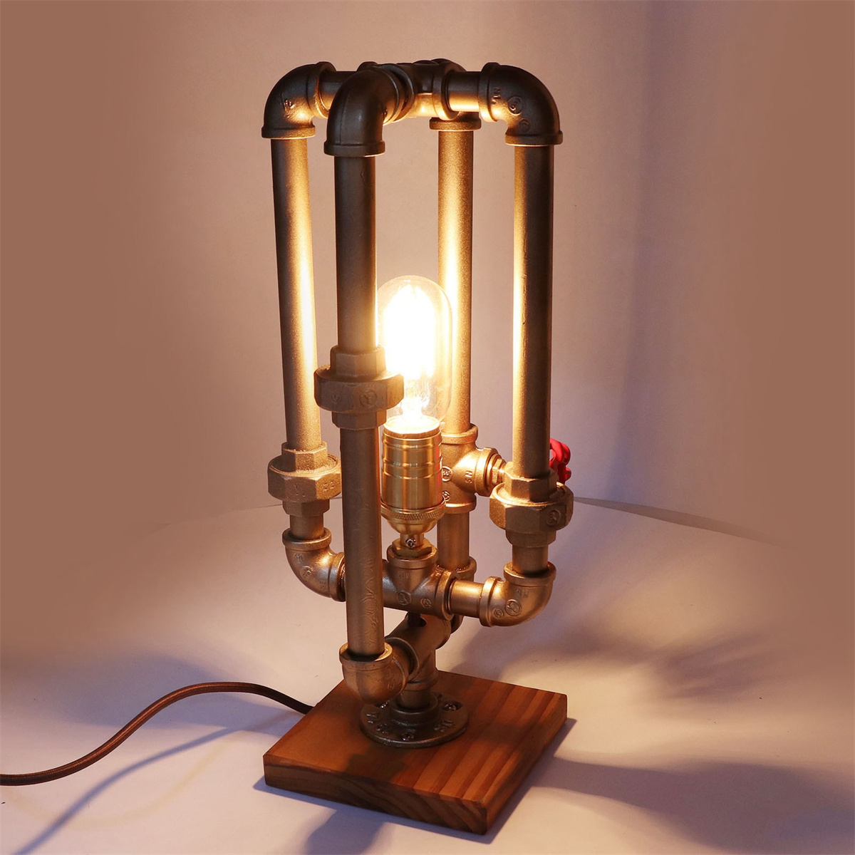 Eine Lampe im Steampunk-Stil aus Kupferrohren mit Glühbirne steht auf einem Holzsockel.