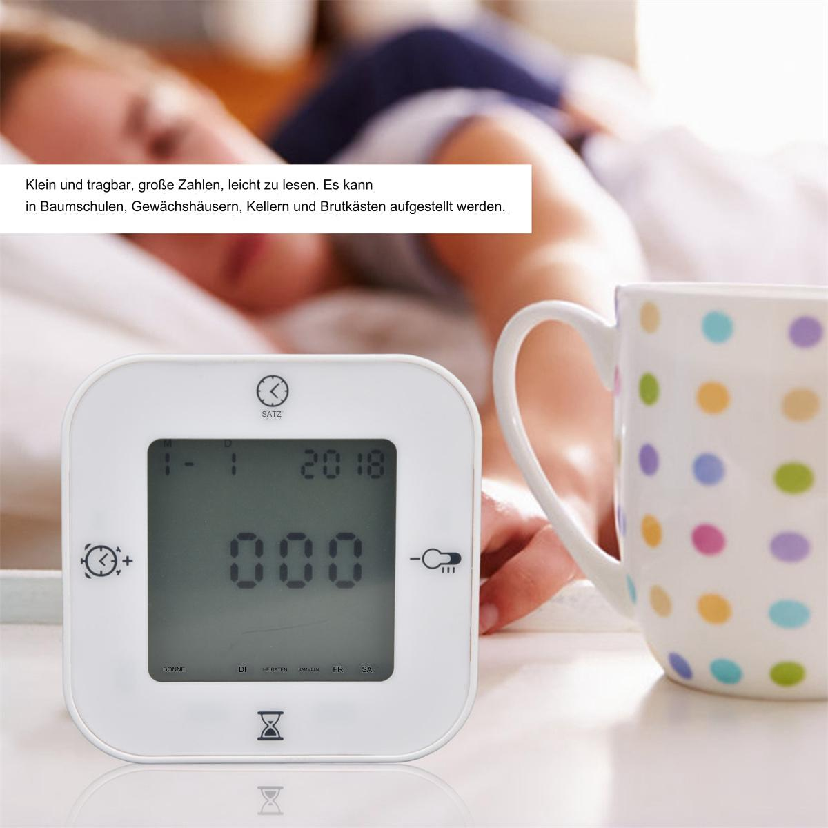Weiße Digitaluhr mit Text, eine Person im Bett und eine Tasse mit bunten Tupfen auf einem Tisch.