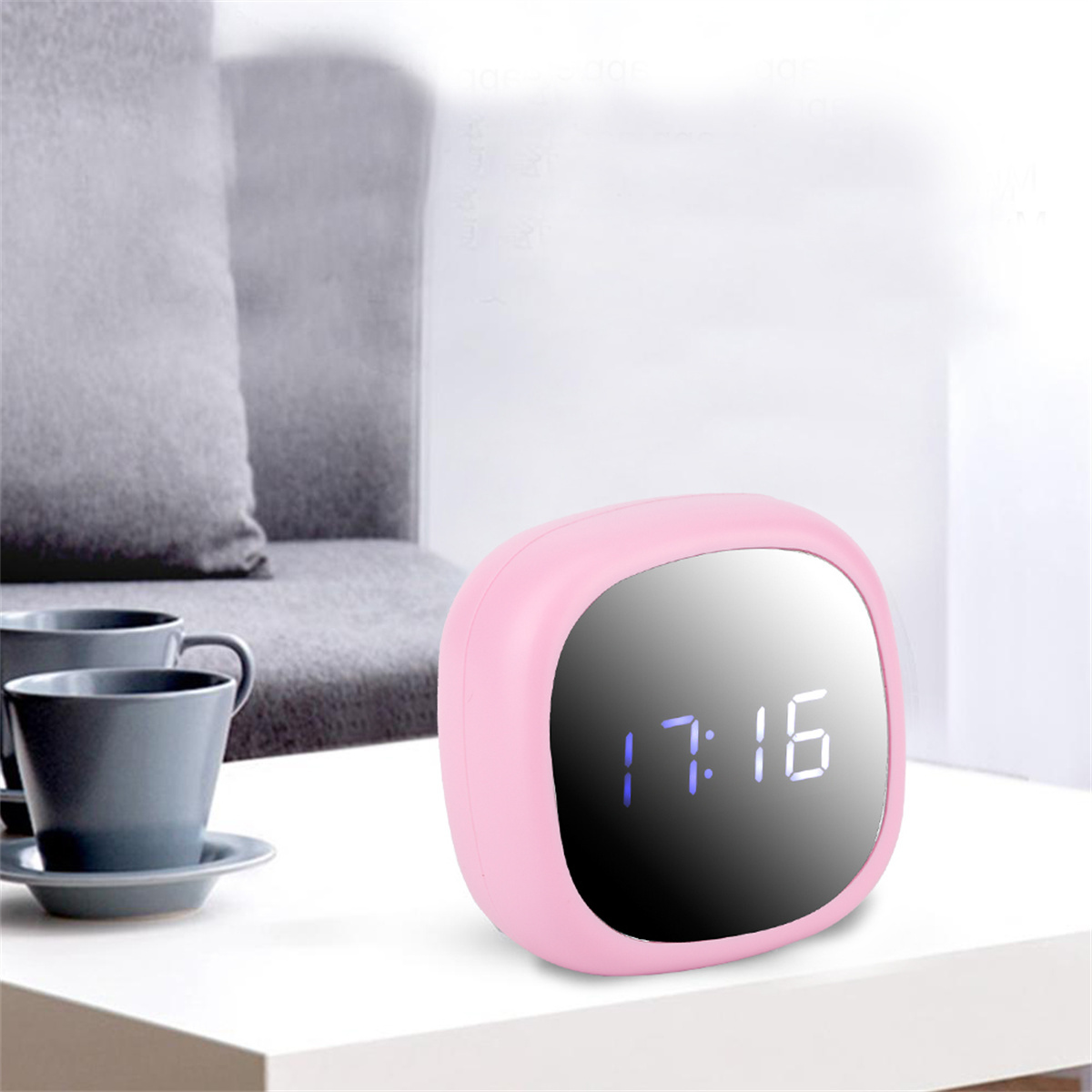 Ein rosa Wecker zeigt 17:16 auf dem Bildschirm. Zwei graue Tassen und ein Sofa sind im Hintergrund.