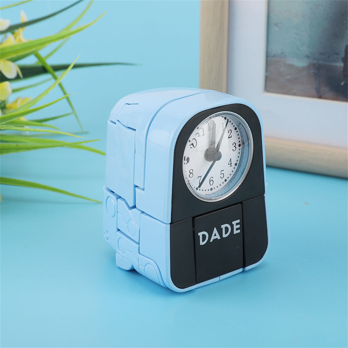 Ein blauer, sich verwandelnder Wecker mit einem schwarzen Bildschirm, auf dem 'DADE' steht.