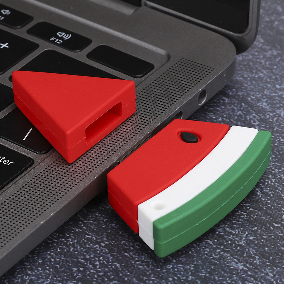 Ein rot-grüner USB-Stick in Wassermelonenform und seine rote Kappe liegen auf einer Laptop-Tastatur.