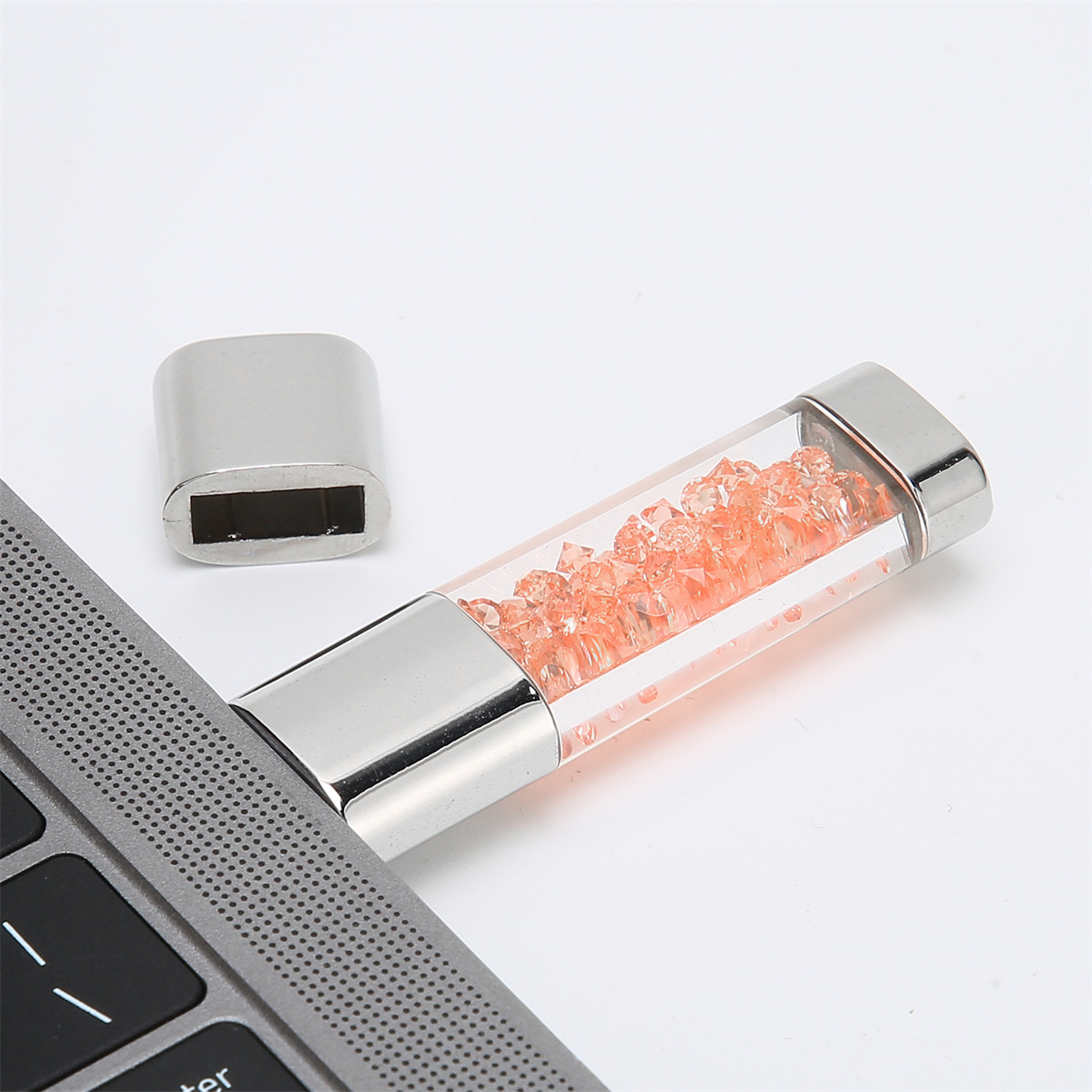 Ein USB-Stick gefüllt mit orangen Kristallen, neben einer Laptop-Tastatur.