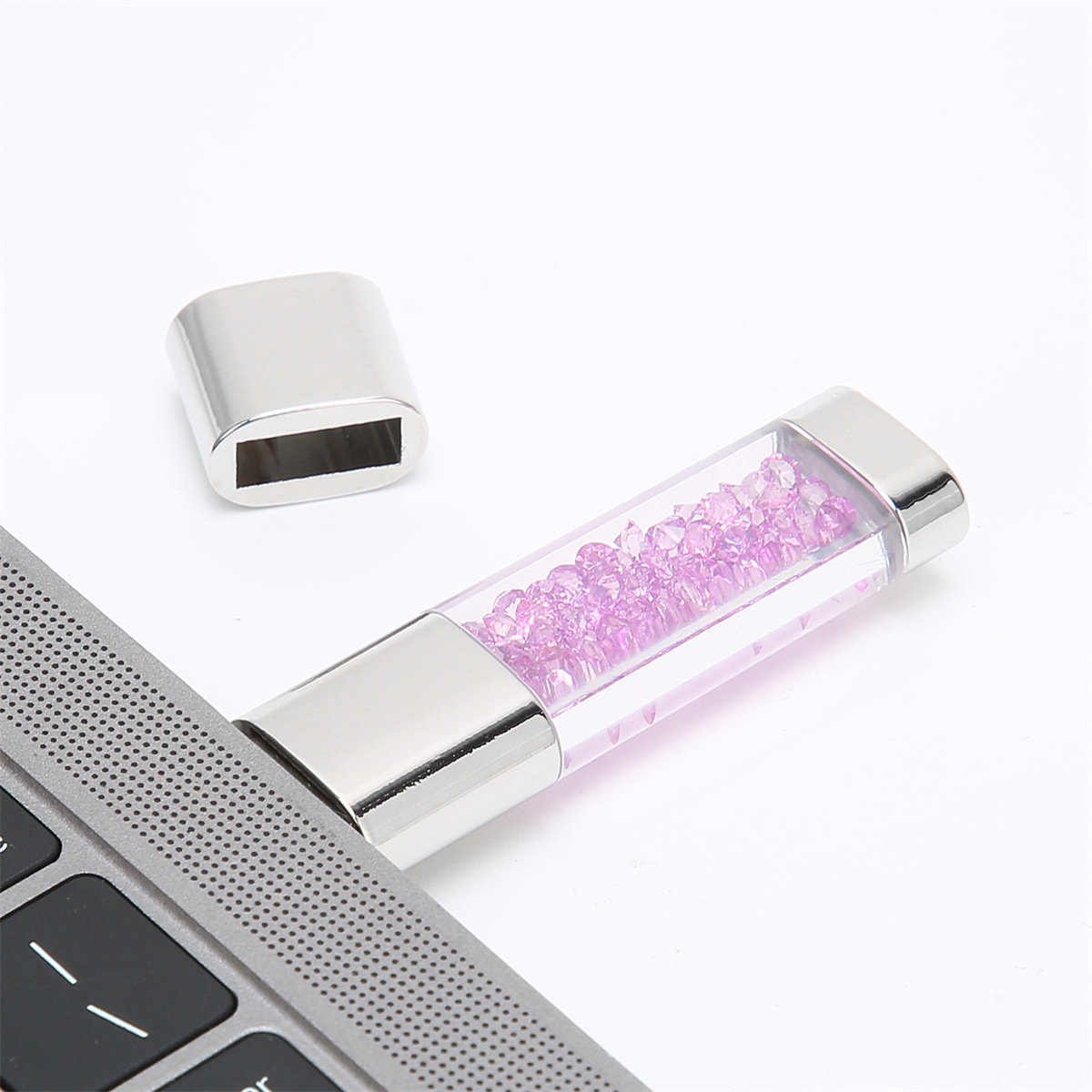USB-Stick mit rosa Kristallen, Silbergehäuse, auf einem Laptop.