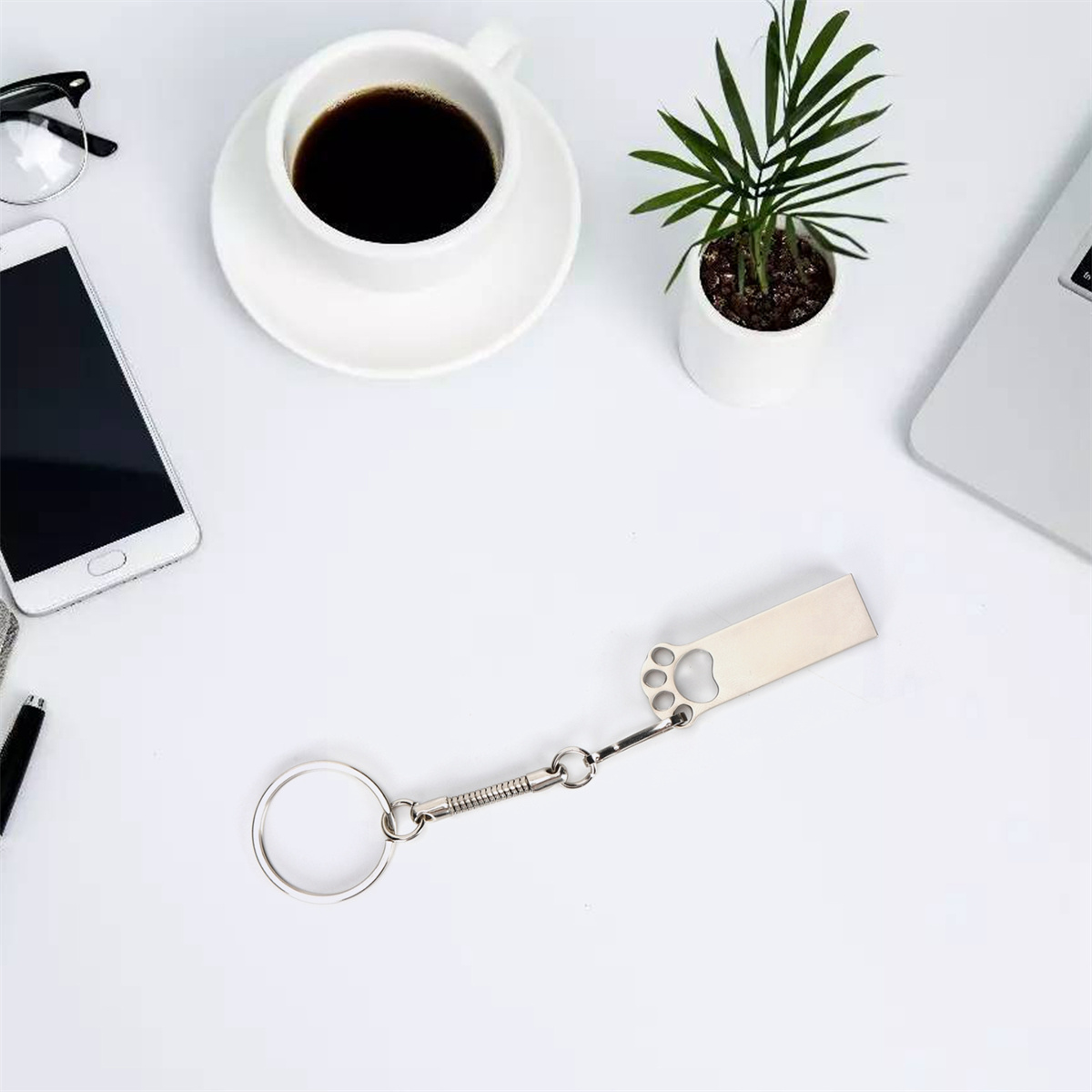 Weißer Schreibtisch: Kaffee, Telefon, Brille, Stift, ein Pfotenabdruck-Schlüsselanhänger und eine kleine Pflanze.