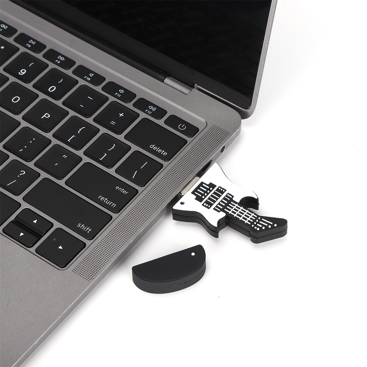 Gitarrenförmiger USB-Stick, der in einen Laptop eingesteckt ist, mit seiner Kappe daneben.