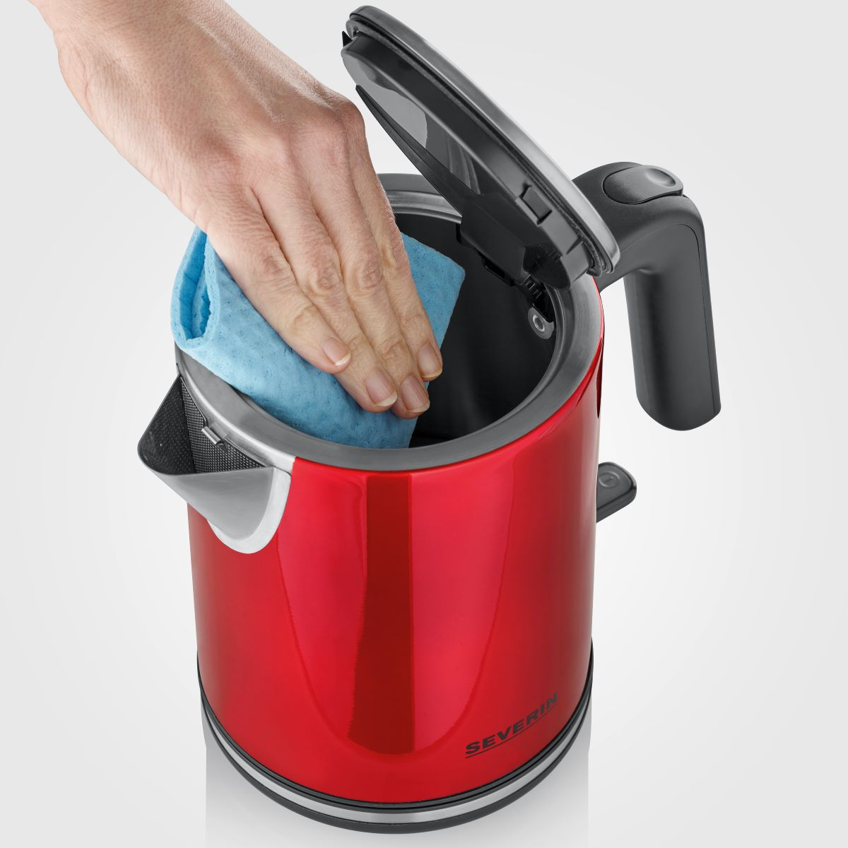Osoba czyszcząca wnętrze czerwonego czajnika elektrycznego niebieską szmatką.