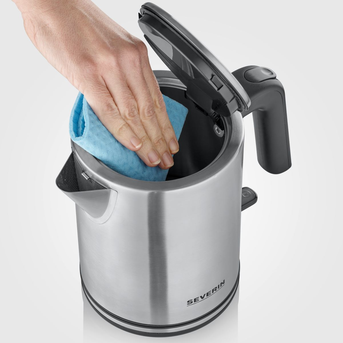 Ręka czyszcząca czajnik ze stali nierdzewnej niebieską szmatką.