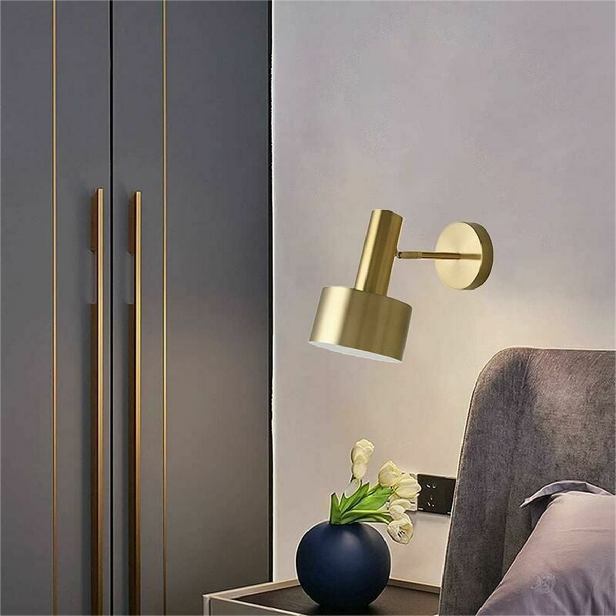 Goldene Wandleuchte an einer Wand. Eine marinefarbene Vase mit Blumen im Vordergrund.
