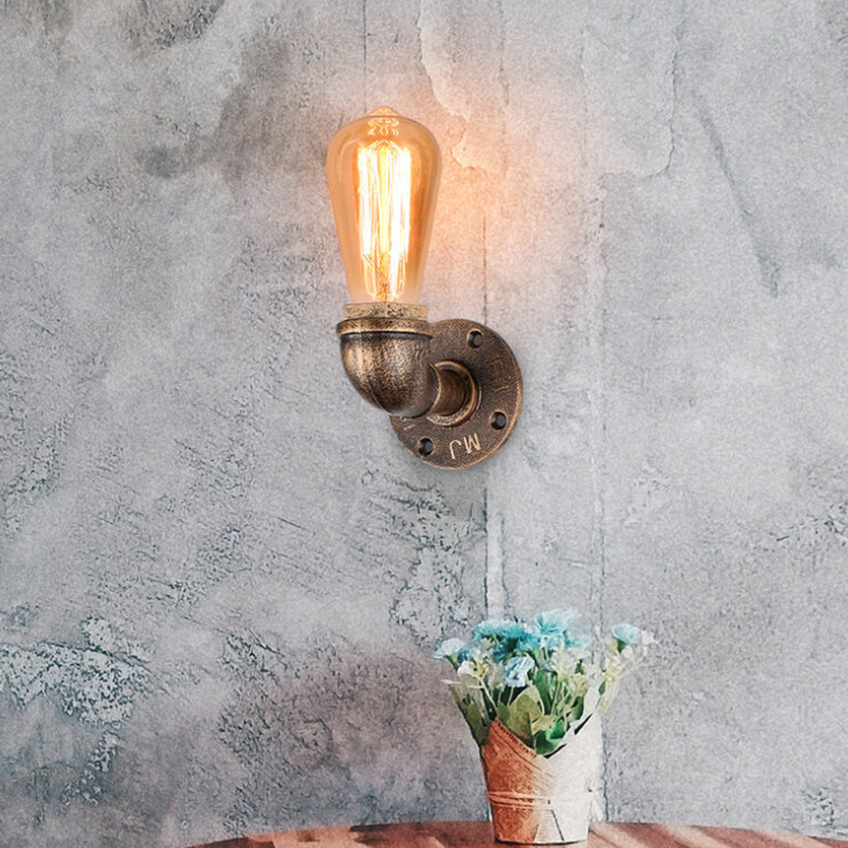 Eine Glühbirne im Edison-Stil ist an einer Wand mit einem metallischen Rohrfitting befestigt. Darunter ein Blumenstrauß.
