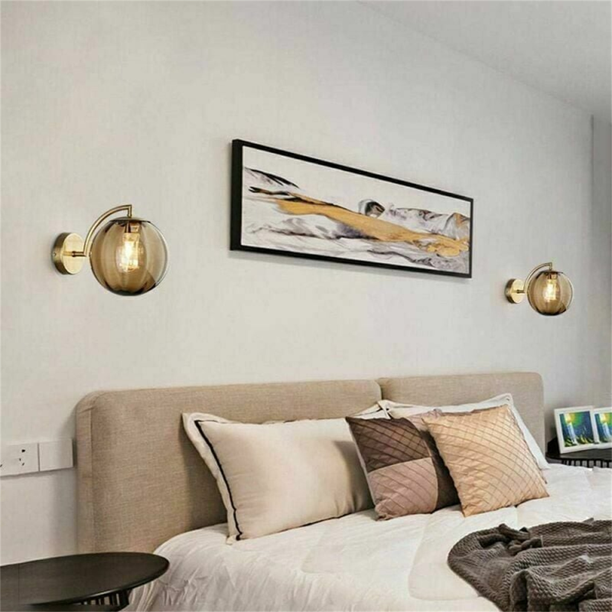 Schlafzimmer mit Bett, gerahmter Kunst und goldenen Wandleuchten.