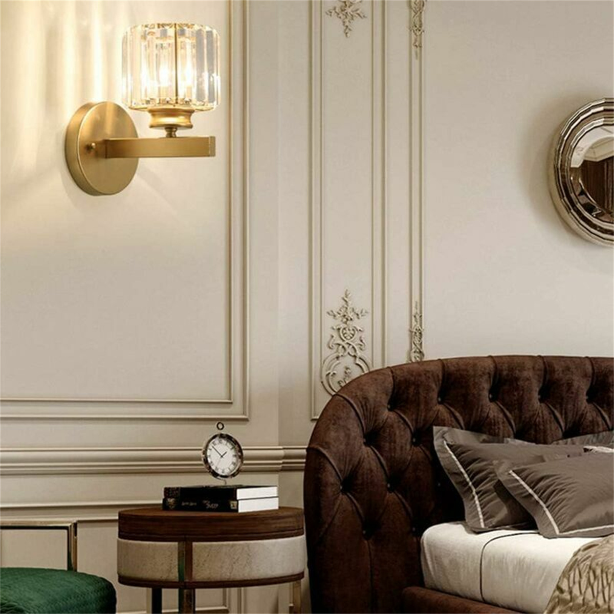 Eine Wandlampe mit Kristallschirm und goldenem Arm. Sie hängt an einer Wand neben einem Bett.