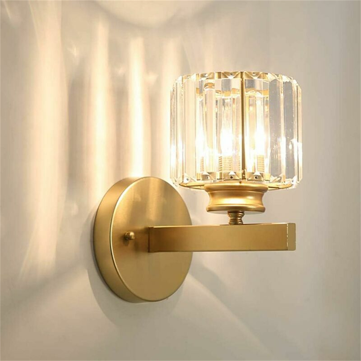 Goldene Wandleuchte, klarer Kristallschirm, beleuchtet weiße Wand.