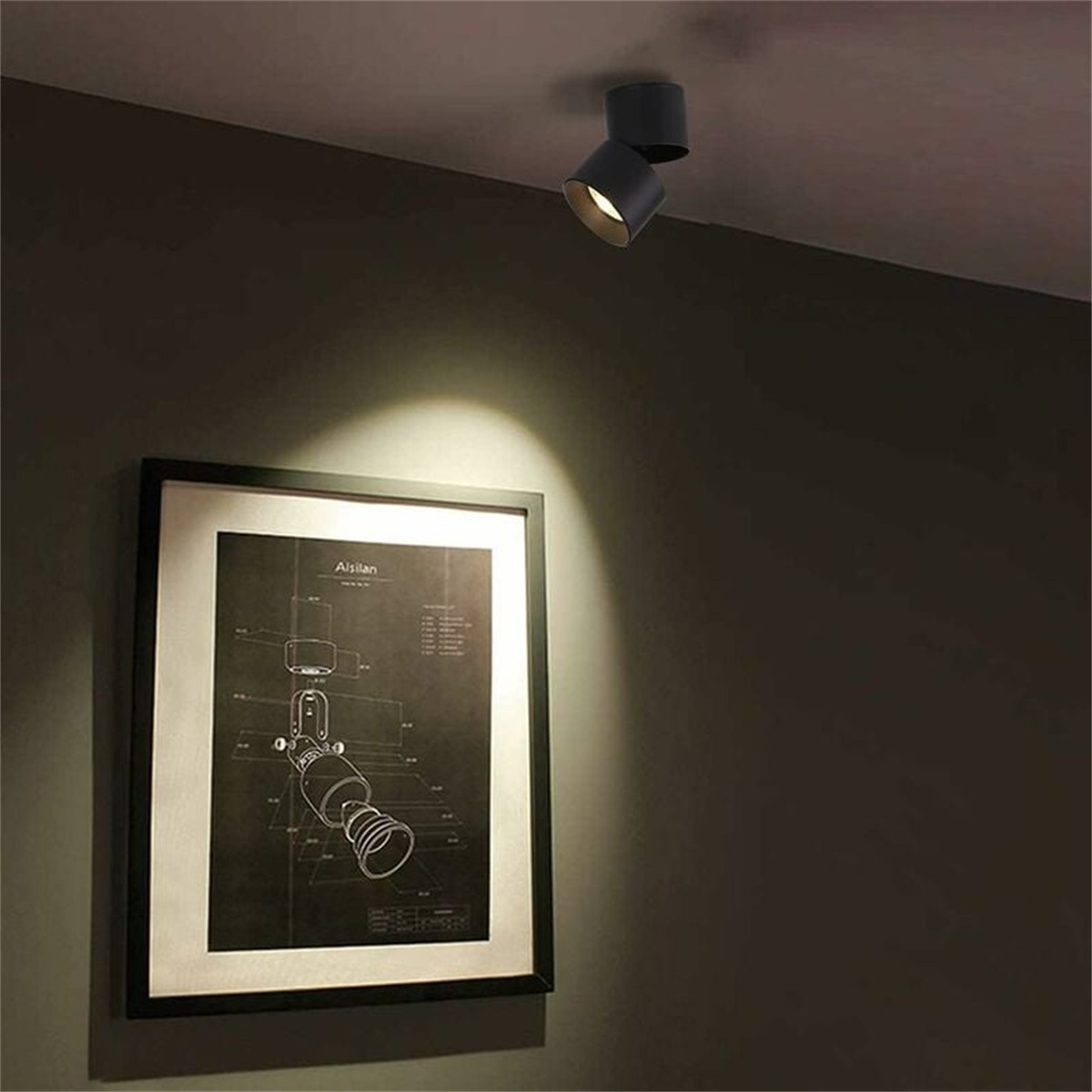 Zwei schwarze Strahler an einer Decke, mit einem gerahmten Bild an der Wand.