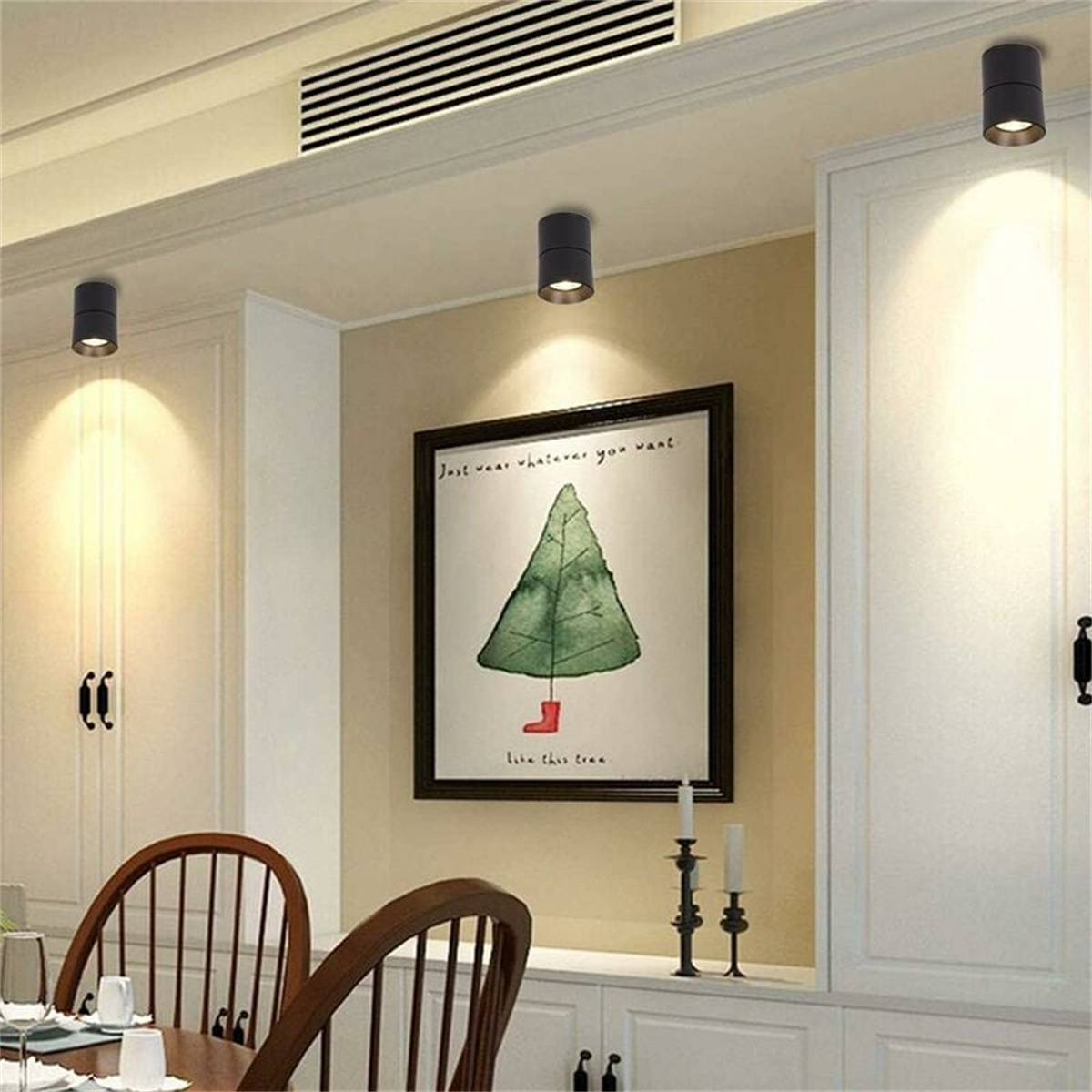 Drei schwarze zylindrische Lampen an einer Decke, mit einem Bild eines Weihnachtsbaums an der Wand.