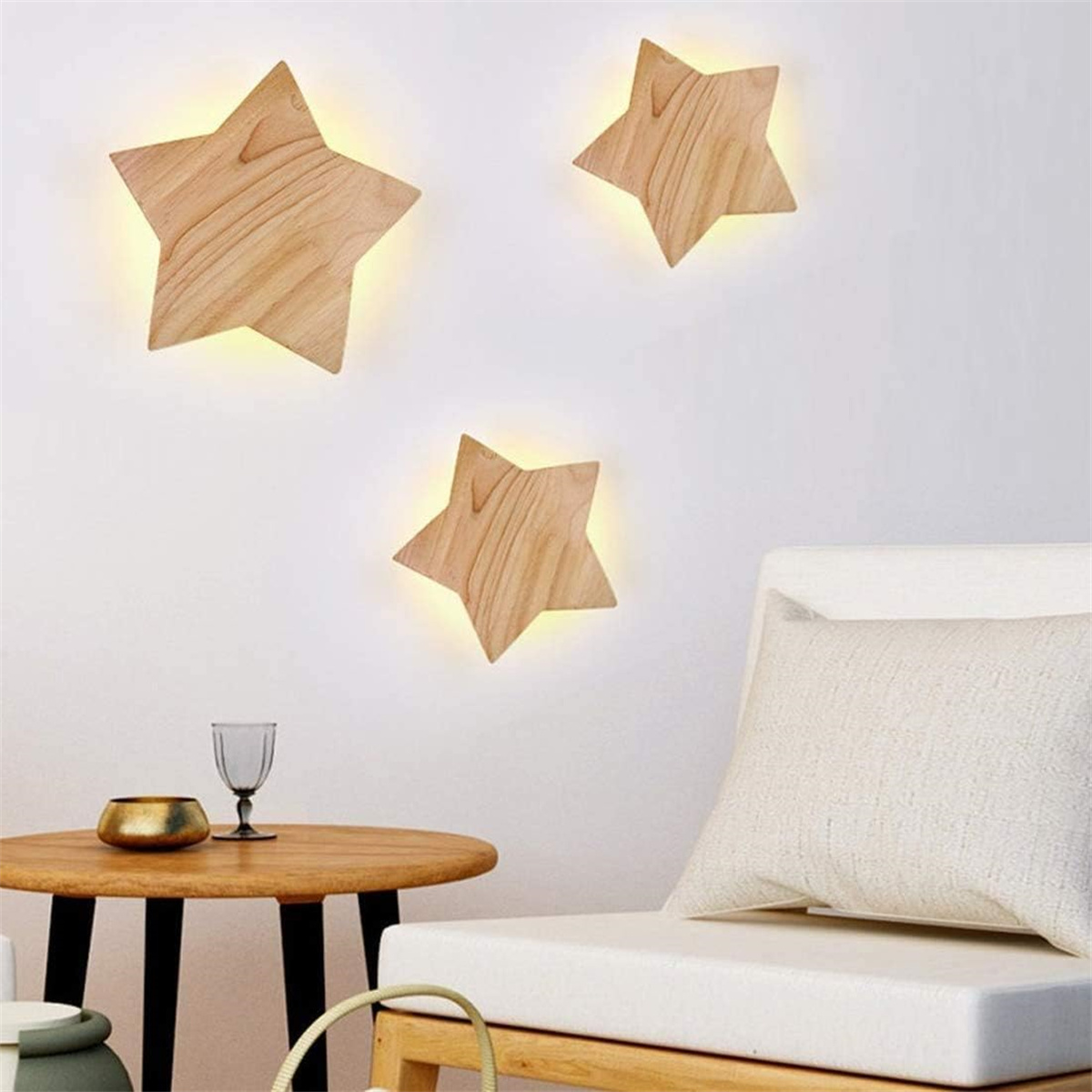 Drei hölzerne Sternlichter an einer weißen Wand. Ein Stuhl und ein Tisch befinden sich im Vordergrund.