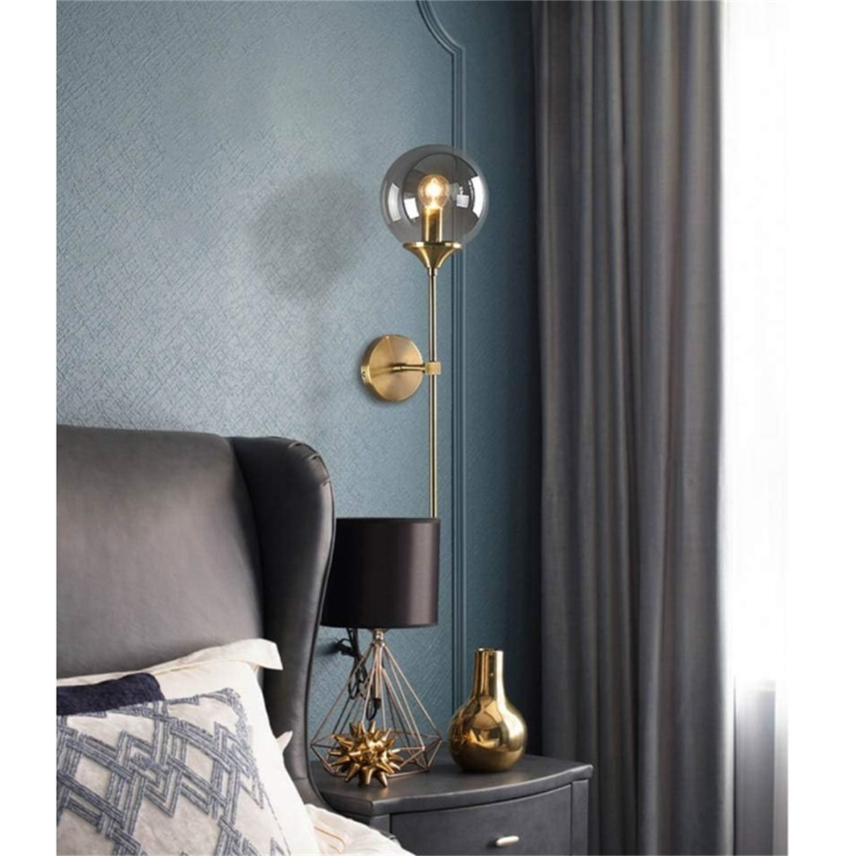 Eine wandmontierte goldene Lampe mit kugelförmigem Glasschirm, neben einer schwarzen Lampe auf einem Nachttisch.