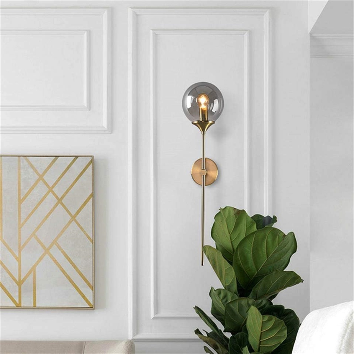 Eine Wandlampe mit Glaskugel, goldener Halterung, an einer weißen Wand mit Pflanze montiert.