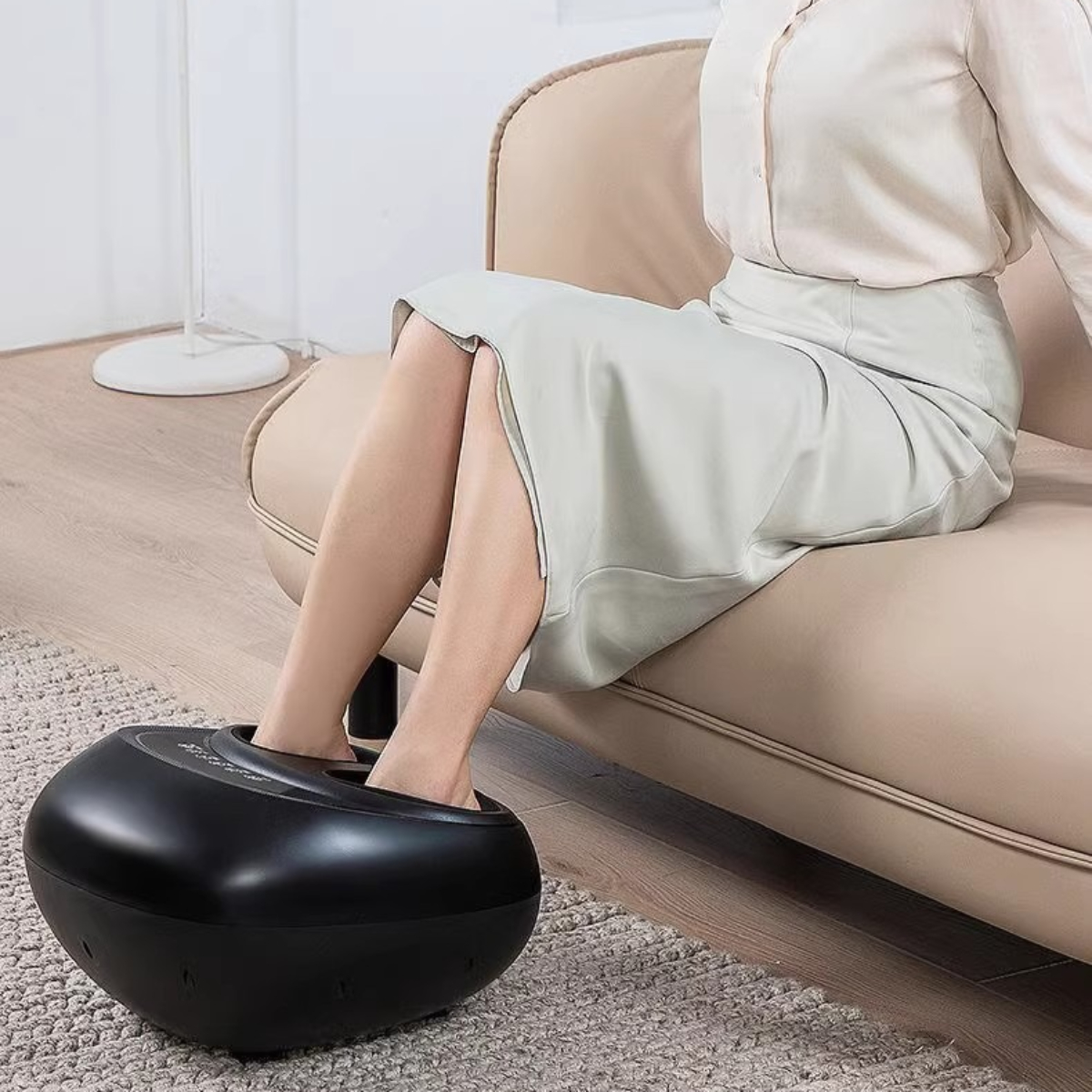 Person nutzt schwarzen Fußmassager, sitzt auf beigem Sofa.