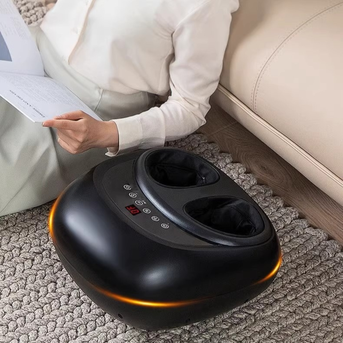 Schwarzes Fußmassagegerät mit Bedienfeld, orangefarbenen Lichtern und eine Person liest ein Buch.