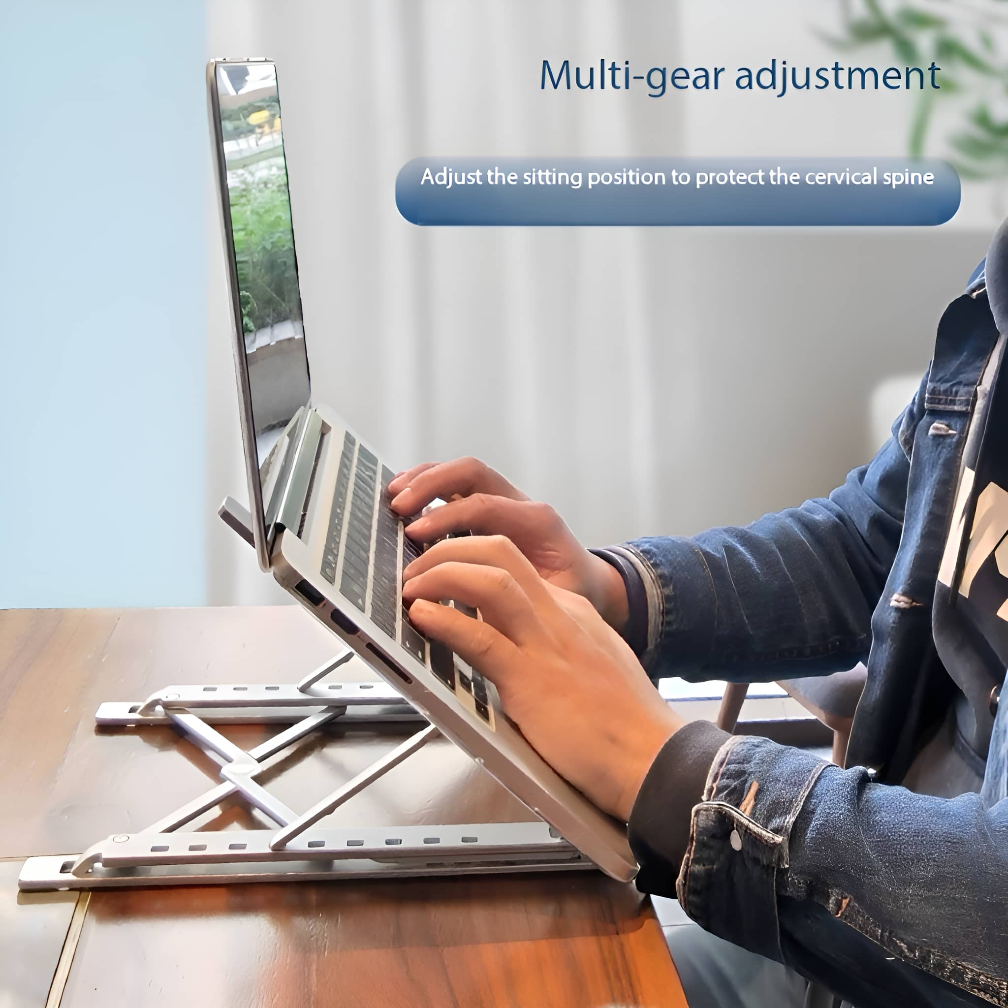 Laptop auf silbernem Ständer, Hände tippen darauf, Tisch im Hintergrund.