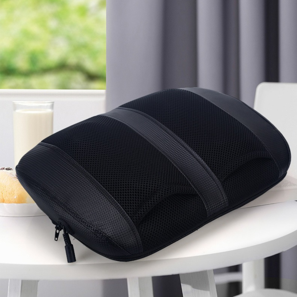 Schwarzes Rückenstützkissen aus Mesh auf einem weißen Tisch. Ein Glas und ein Teller sind auf dem Tisch.