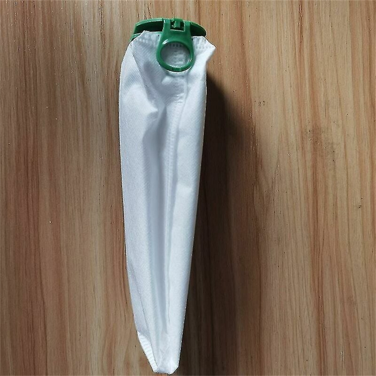Weißer Staubsaugerbeutel mit grünem Clip vor holzhintergrund.