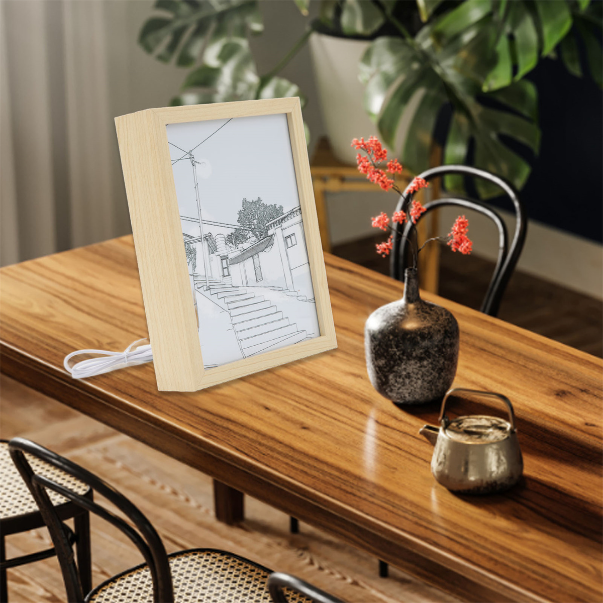 Holzgerahmtes Bild mit Zeichnung auf Holztisch mit Deko und Pflanze.