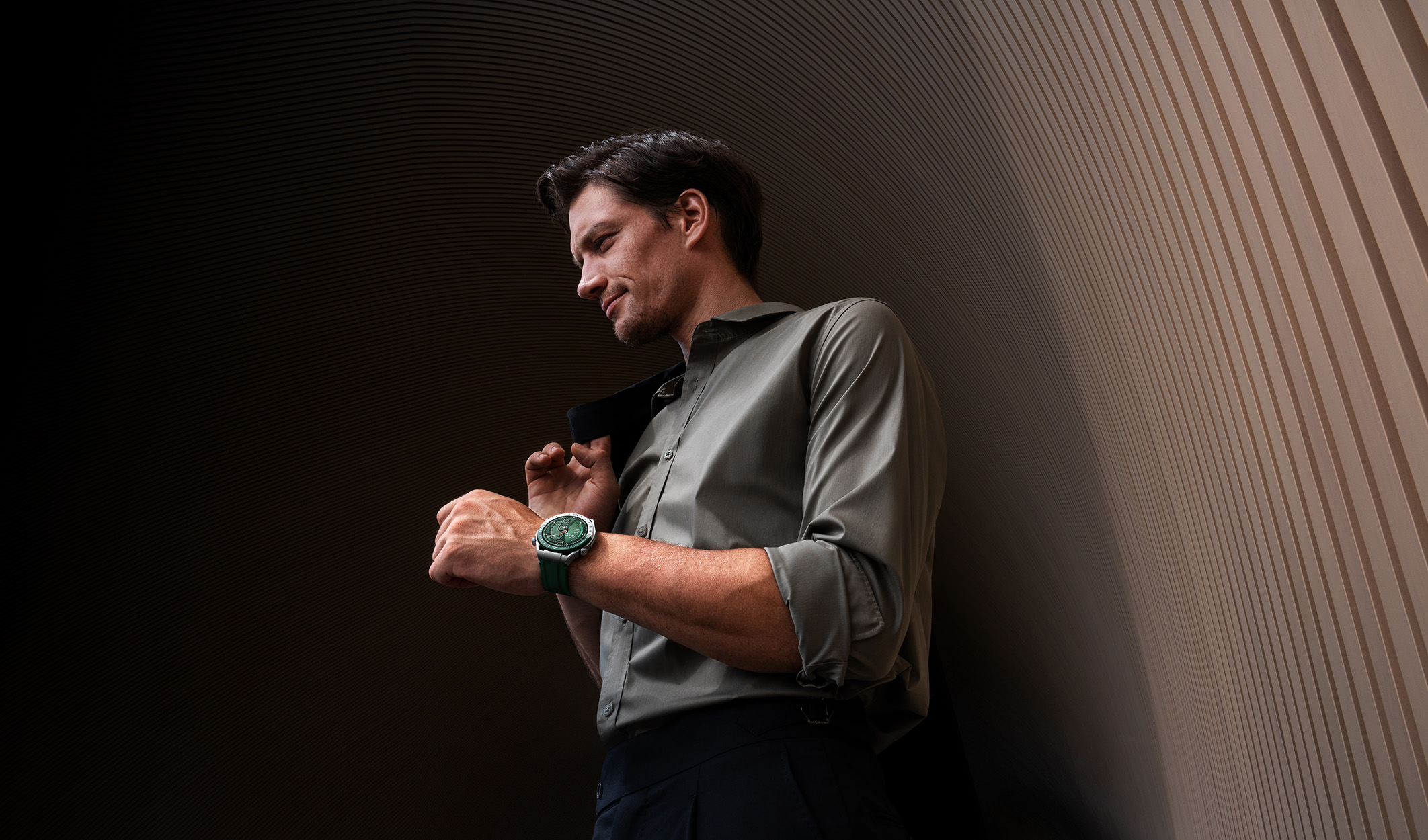 Ein Mann in Hemd und Uhr steht an einer Wand. Er hält eine Jacke über seiner Schulter.