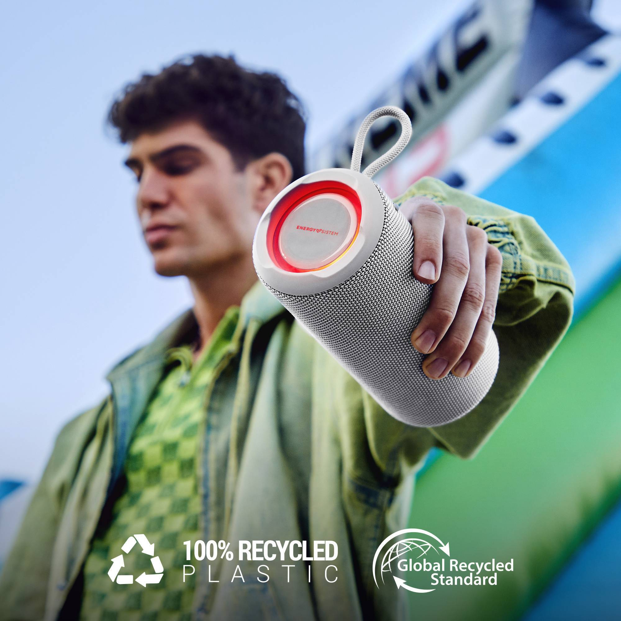 Un hombre sosteniendo un altavoz blanco con un anillo rojo. Dice Energy System y 100% plástico reciclado.