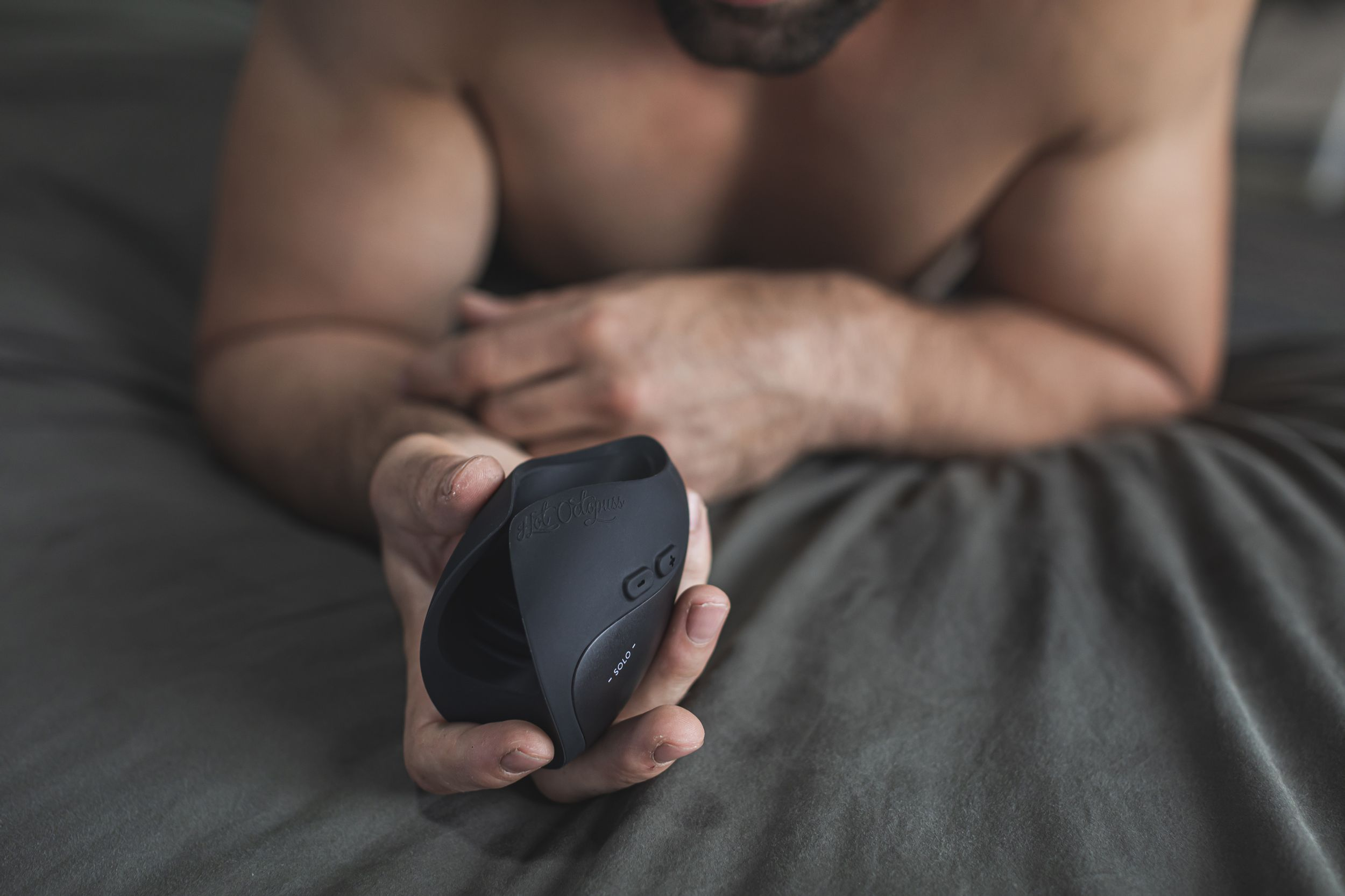 Tułów mężczyzny z czarną zabawką erotyczną w dłoni.