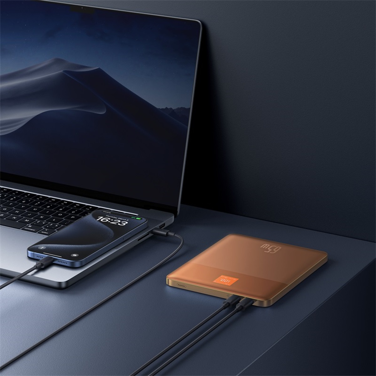 Un laptop e un telefono vengono caricati da un power bank dorato. Il power bank mostra 65W.