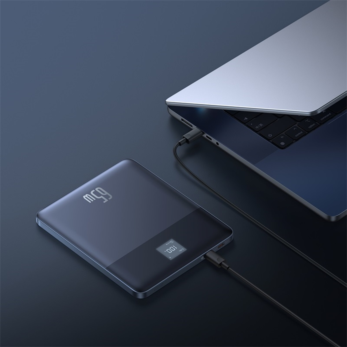 Cargador portátil negro conectado a un portátil. Pantalla muestra 65W y 100%.