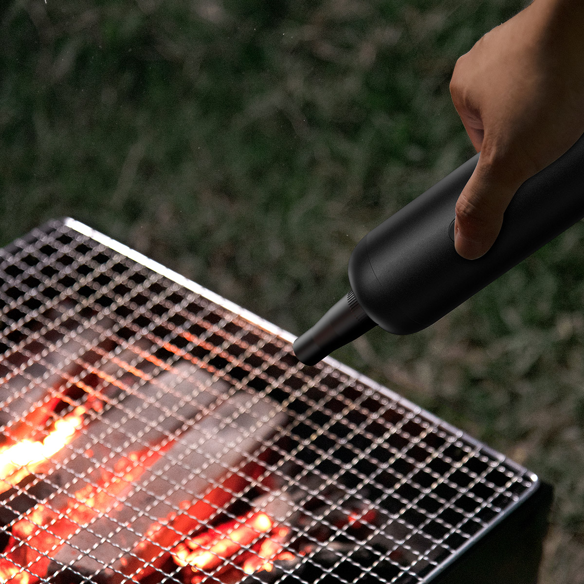 Mano che usa un soffiatore d'aria nero su una griglia. Fiamme e griglia sono visibili.