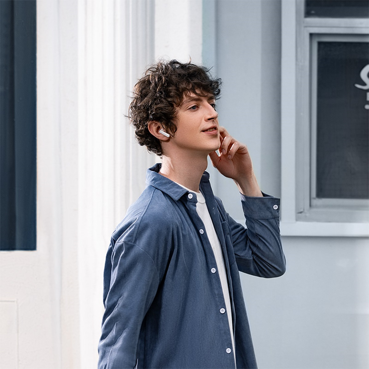 Mężczyzna w białym słuchawce, rozmawiający przez telefon na ulicy. Ma na sobie niebieską koszulę.