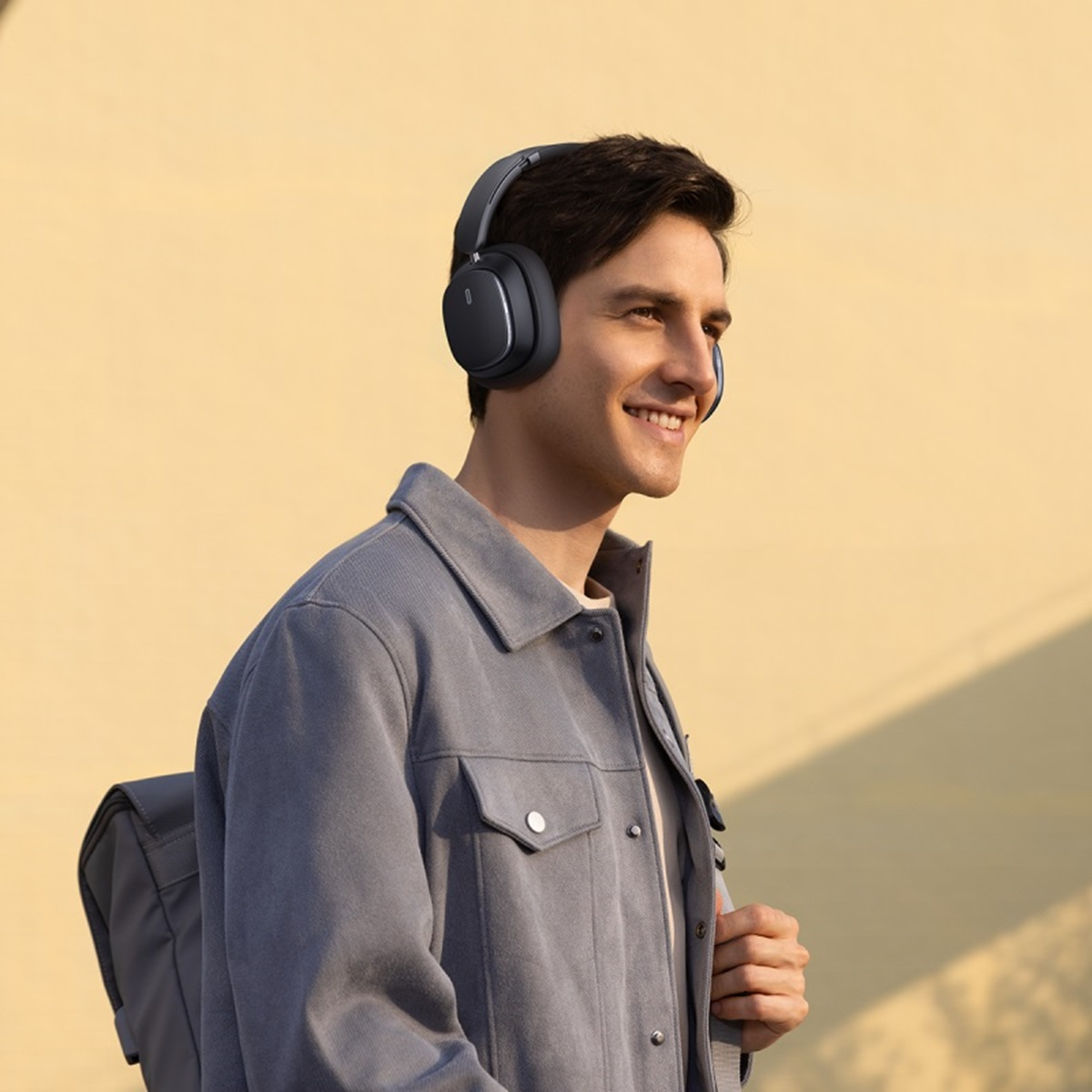 Un uomo con le cuffie che sorride, con uno zaino. Sta camminando fuori.