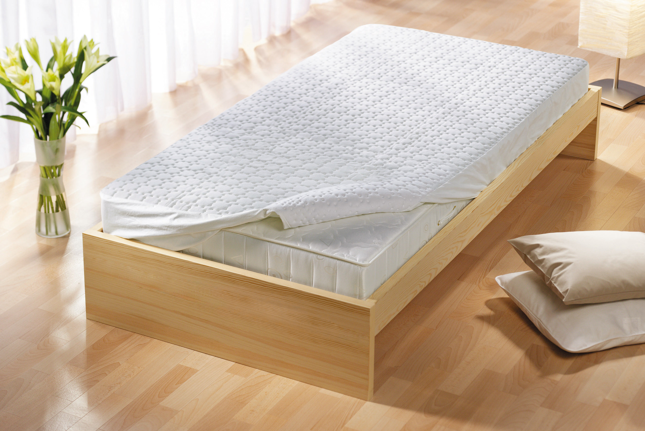 A wooden bed frame with a white mattress and pillows. The floor is wooden.