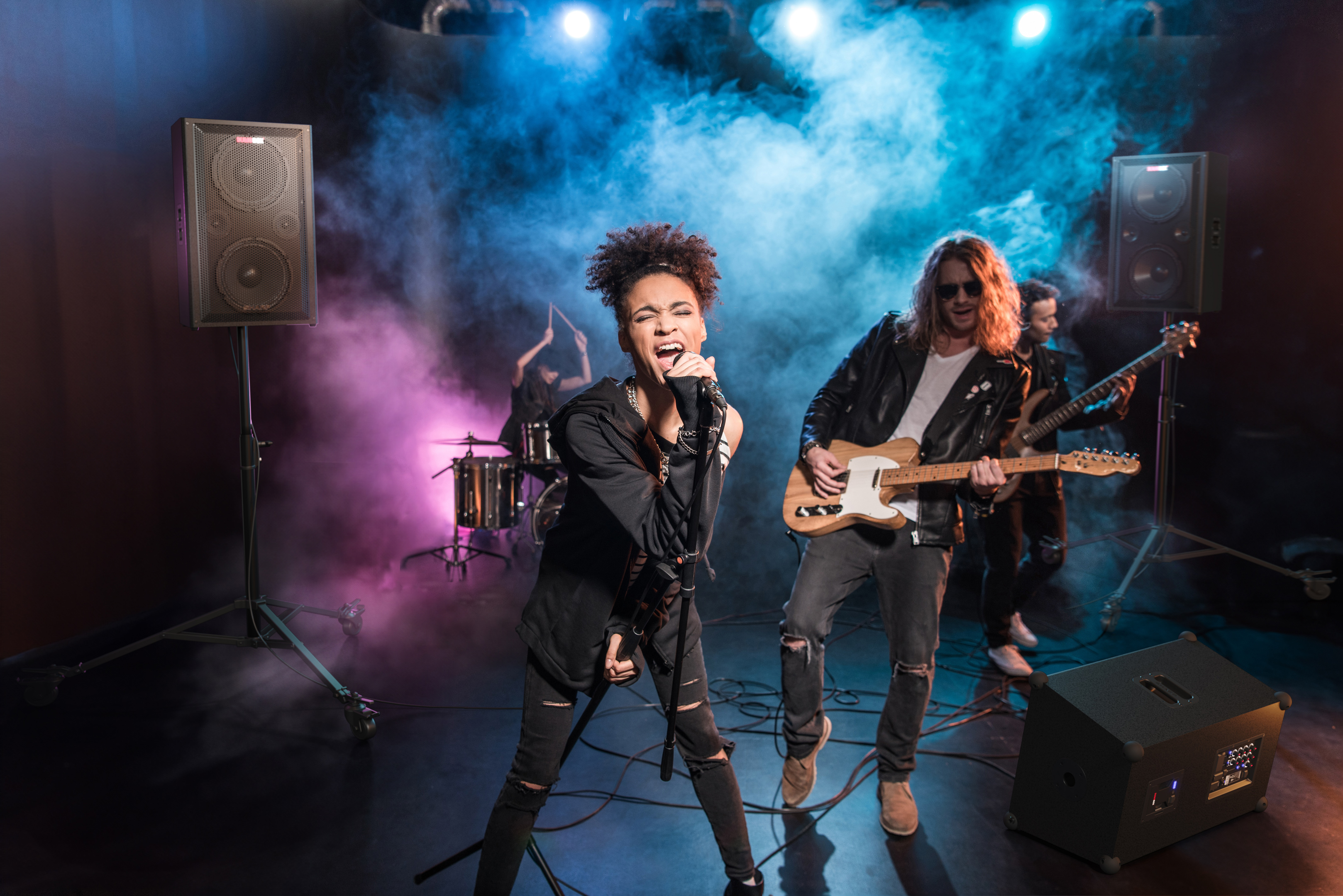 Una band sul palco che si esibisce. Un cantante, un chitarrista, un batterista e altoparlanti.