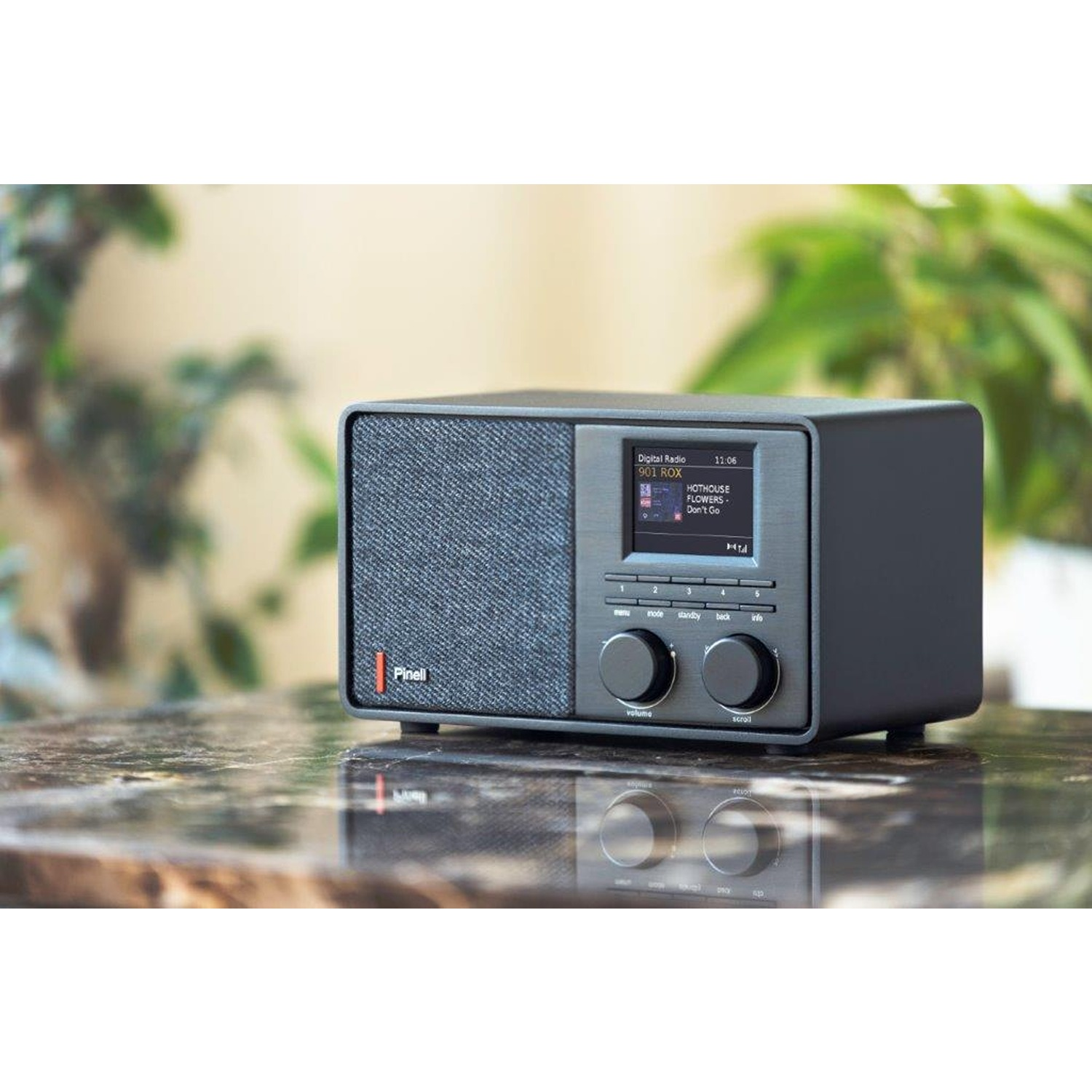 Black and grey radio on a table. It has a small screen and two control knobs. The brand is Pinell.