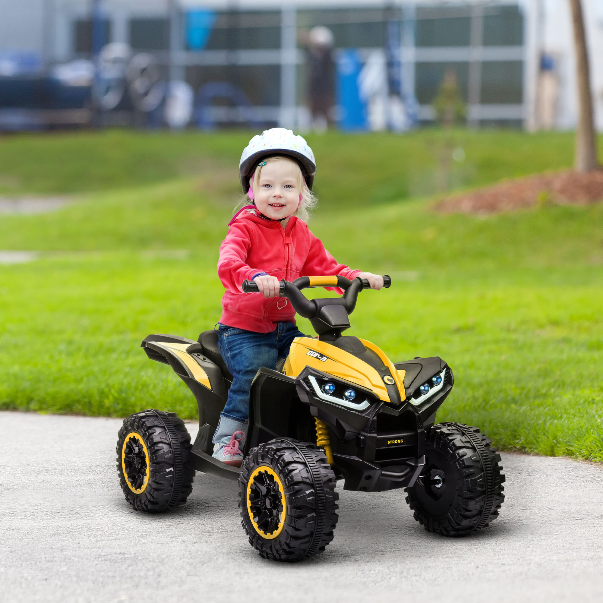 Un niño pequeño en rojo montando un quad amarillo en un camino pavimentado.